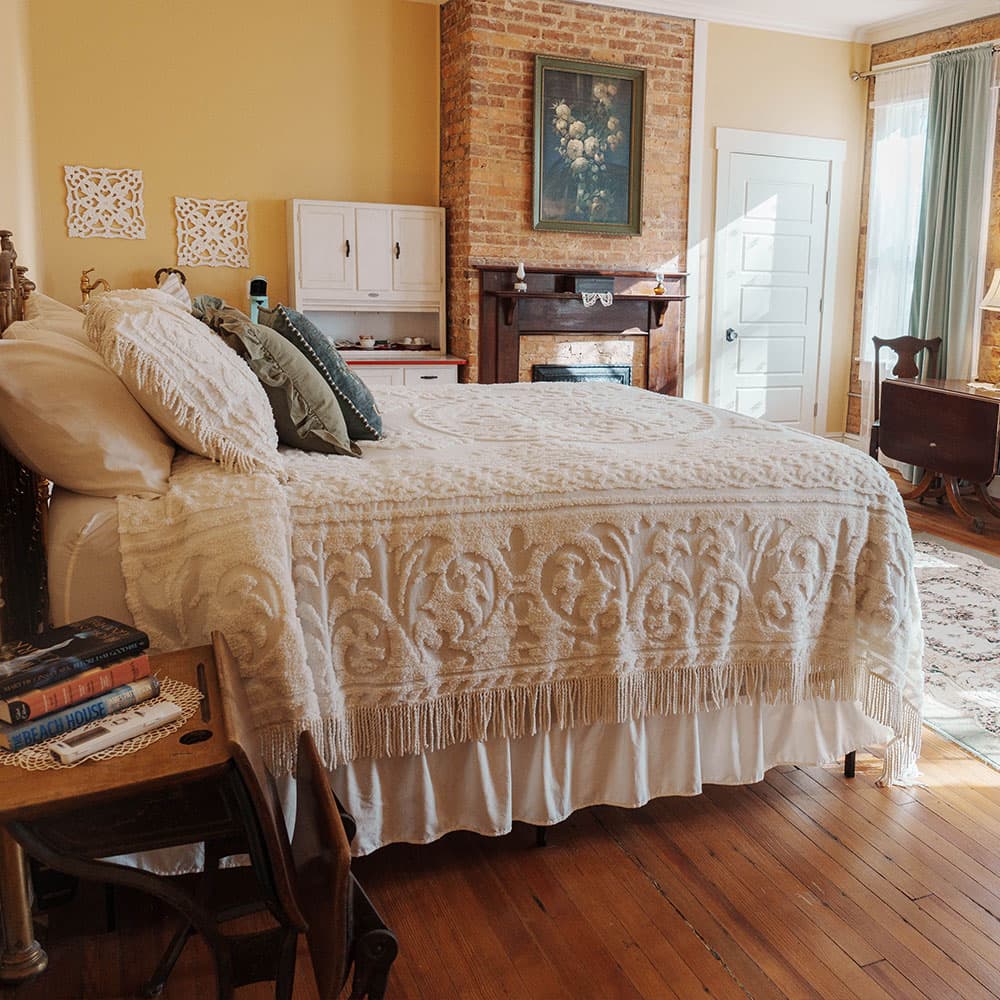 A cozy bedroom featuring a large bed with a textured blanket, a brick wall, and vintage decor elements.